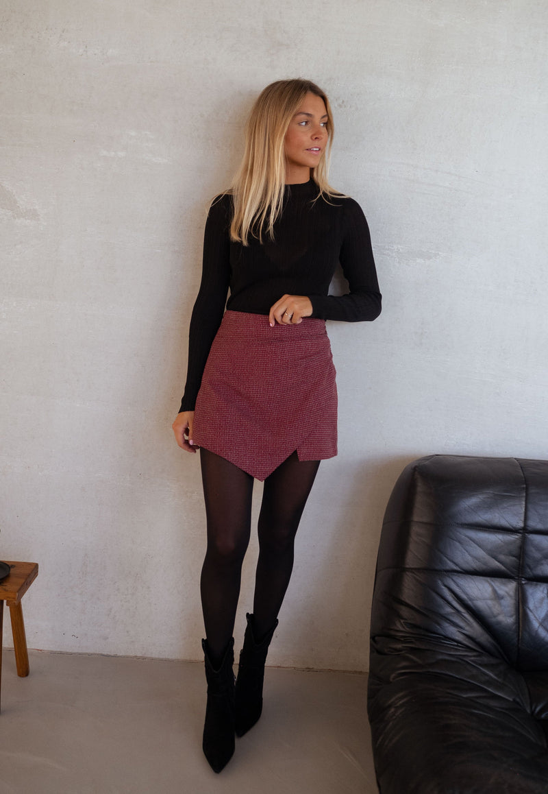 Jupe-short à carreaux drapée porté par une femme, silhouette entière, haut noir, collants