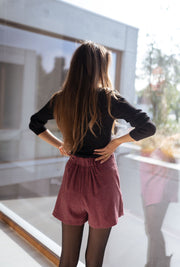 Jupe-short à carreaux drapée porté par une femme, vue de dos, baie vitrée, bras sur les hanches