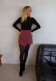 Jupe-short à carreaux drapée porté par une femme, silhouette entière, haut noir, mur blanc