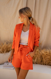 Short court à détails dorés porté par une femme, vue de trois-quarts, blazer orange, paille