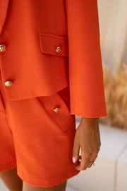 Short court à détails dorés porté par une femme, vue rapprochée, blazer orange, boutons dorés