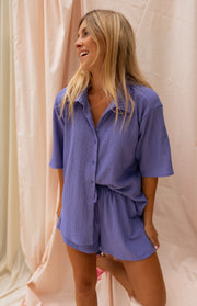 Short court fluide porté par une femme, vue de trois-quarts, rideau rose, sourire