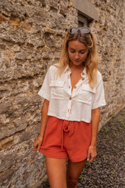 Short court à taille élastique porté par une femme, vue de trois-quarts, chemise blanche, short brique