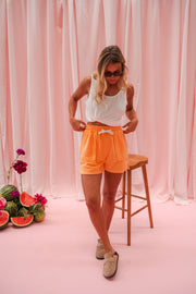 Short éponge à cordon porté par une femme, silhouette entière, débardeur blanc, tabouret