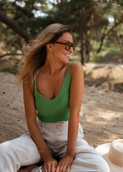 Top en maille décolleté V porté par une femme, assise, sable, lunettes de soleil