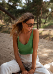 Top en maille décolleté V porté par une femme, vue de trois-quarts, lunettes de soleil, sable