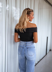 Body bustier à épaules dégagées porté par une femme, vue de dos, rideaux, jean