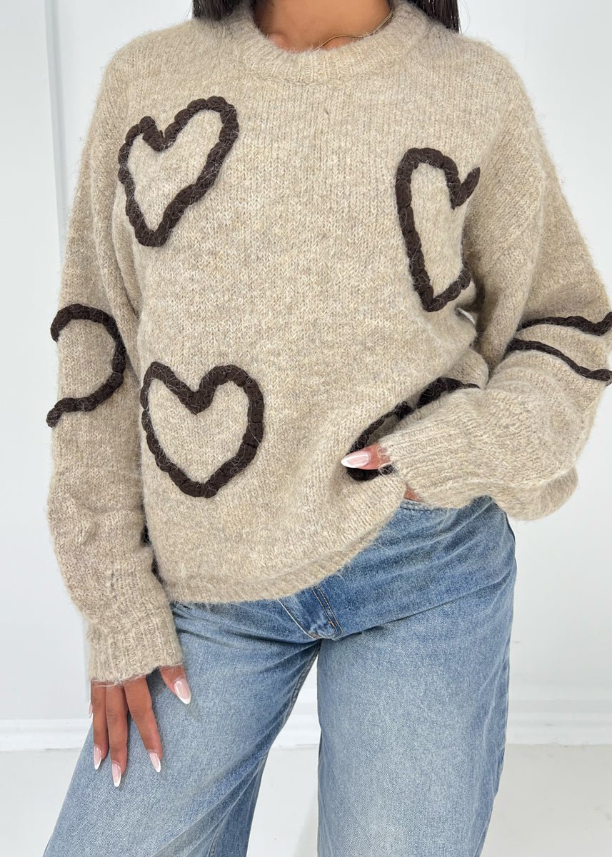 Pull beige à motif cœurs — vue portée de face, cadrée à la taille, légèrement de côté, grands cœurs noirs
