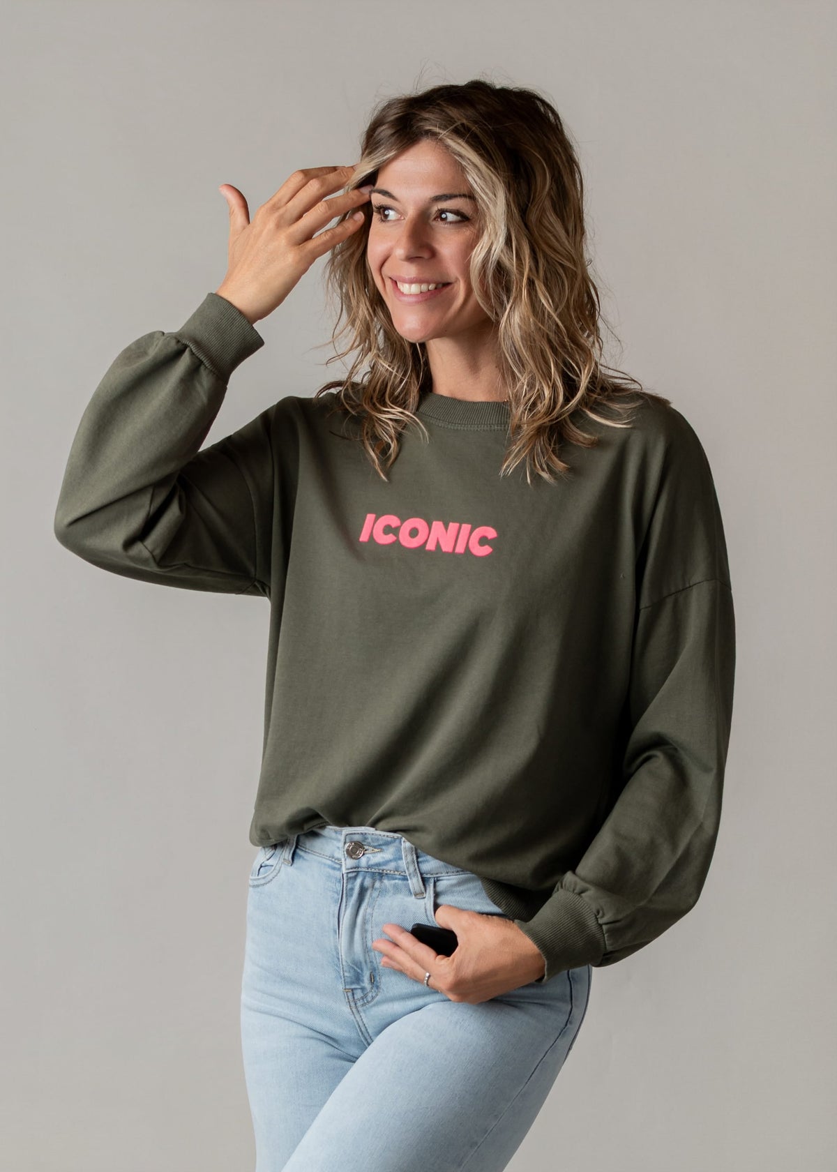 Sweat fin en coton porté par une femme, vue de trois-quarts, main sur la tête, jean