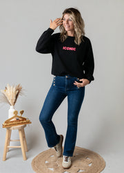 Sweat fin en molleton porté par une femme, silhouette entière, jean flare, main sur la tête