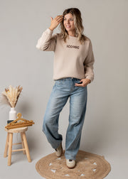 Jean coupe ballon délavé porté par une femme, silhouette entière, pull beige, tabouret