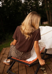 T-shirt large col rond chocolat porté par une femme, vue de dos, terrasse, plaid