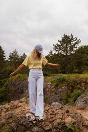 T-shirt ample col rond jaune porté par une femme, silhouette entière, rochers, pantalon blanc