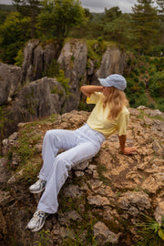 T-shirt ample col rond jaune porté par une femme, assise, rochers, baskets