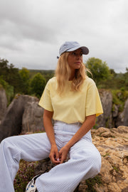 T-shirt ample col rond jaune porté par une femme, assise, rochers, casquette