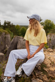 T-shirt ample col rond jaune porté par une femme, assise, rochers, pantalon blanc