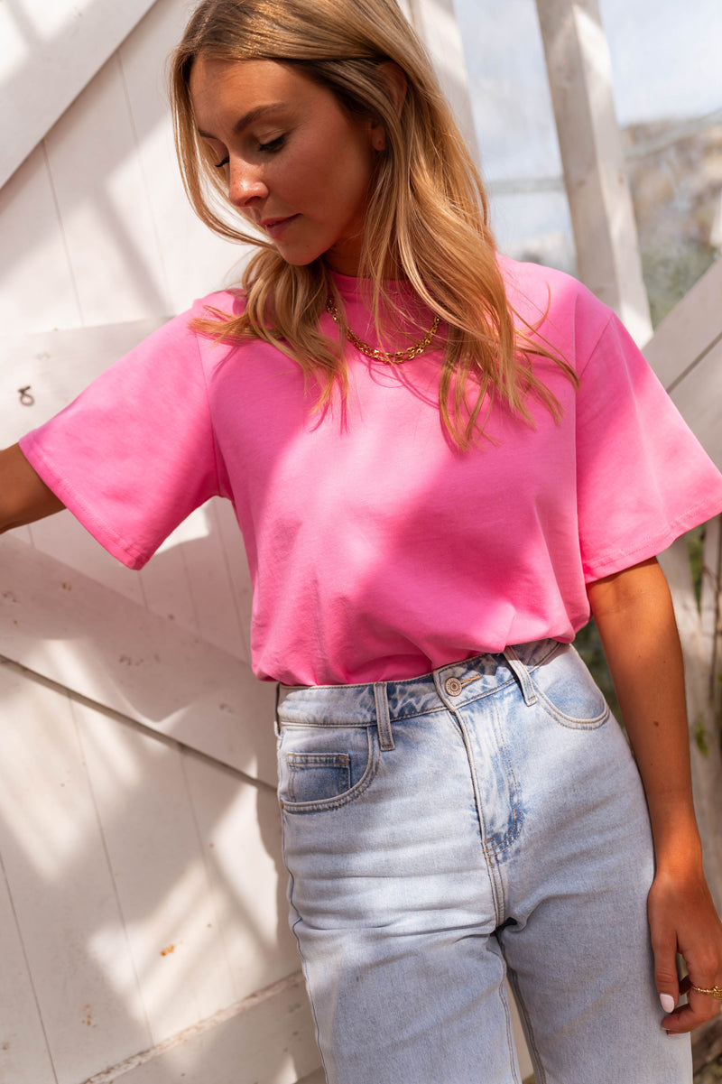 T-shirt ample manches courtes rose porté par une femme, vue de face, mur blanc, jean clair
