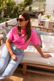 T-shirt ample manches courtes rose porté par une femme, assise, canapé en bois, lunettes