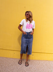 T-shirt doux col rond porté par une femme, silhouette entière, mur jaune, jupe en jean