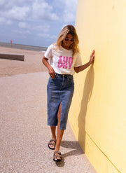 T-shirt doux col rond porté par une femme, silhouette entière, plage, mur jaune