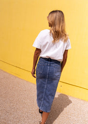 T-shirt doux col rond porté par une femme, vue de dos, mur jaune, jupe en jean