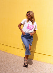 T-shirt doux col rond porté par une femme, vue de trois-quarts, appuyée au mur jaune, baskets
