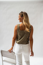 Top fluide col carré porté par une femme, vue de trois-quarts, pantalon blanc, chaise