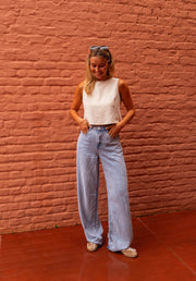 Top fluide effet lin beige porté par une femme, silhouette entière, mur de briques, jean large