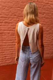 Top fluide effet lin beige porté par une femme, vue de dos, mur de briques, jean clair