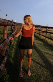 Top doux à décolleté carré porté par une femme, silhouette entière, short noir, herbe