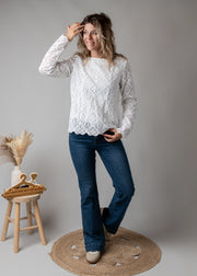 Top dentelle géométrique doublé porté par une femme, vue de trois-quarts, main sur la tête, jean flare