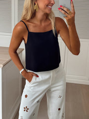 Top dos ouvert col droit porté par une femme, vue de trois-quarts, téléphone, pantalon blanc brodé
