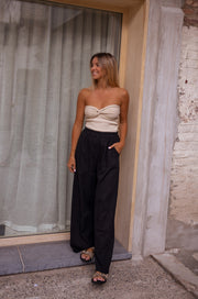 Top bustier à nœud porté par une femme, silhouette entière, rideaux gris, pantalon noir