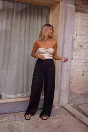 Top bustier à nœud porté par une femme, silhouette entière, façade en brique, rideau