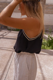 Top fluide à finition crochet porté par une femme, vue de trois-quarts, main dans les cheveux, pantalon blanc