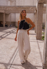 Top fluide à finition crochet porté par une femme, silhouette entière, piliers en béton, pantalon blanc