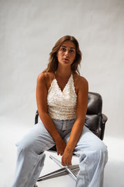 Top pailleté dos ouvert porté par une femme, assise, fauteuil noir, jean clair