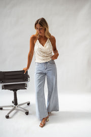 Top pailleté dos ouvert porté par une femme, silhouette entière, fauteuil, jean large