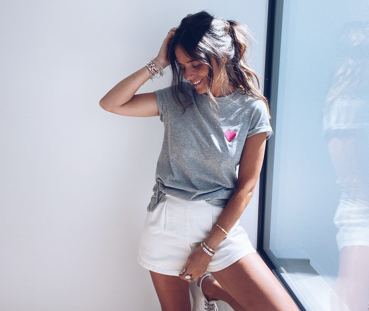 T-shirt à motif cœur porté par une femme, vue de trois-quarts, short blanc, main dans les cheveux