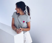 T-shirt à motif cœur porté par une femme, assise, sur un rebord de fenêtre, short blanc