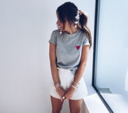 T-shirt à motif cœur porté par une femme, vue de trois-quarts, fenêtre, short blanc