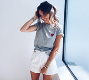 T-shirt à motif cœur porté par une femme, vue de trois-quarts, main dans les cheveux, short blanc