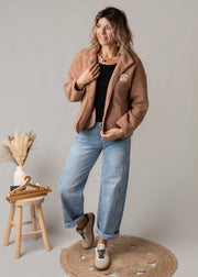 Veste bouclette doublée polaire portée par une femme, silhouette entière, jean large, tabouret
