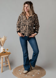 Veste bouclée zippée léopard portée par une femme, silhouette entière, jean flare, tabouret