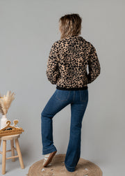 Veste bouclée zippée léopard portée par une femme, vue de dos, jean flare, tabouret
