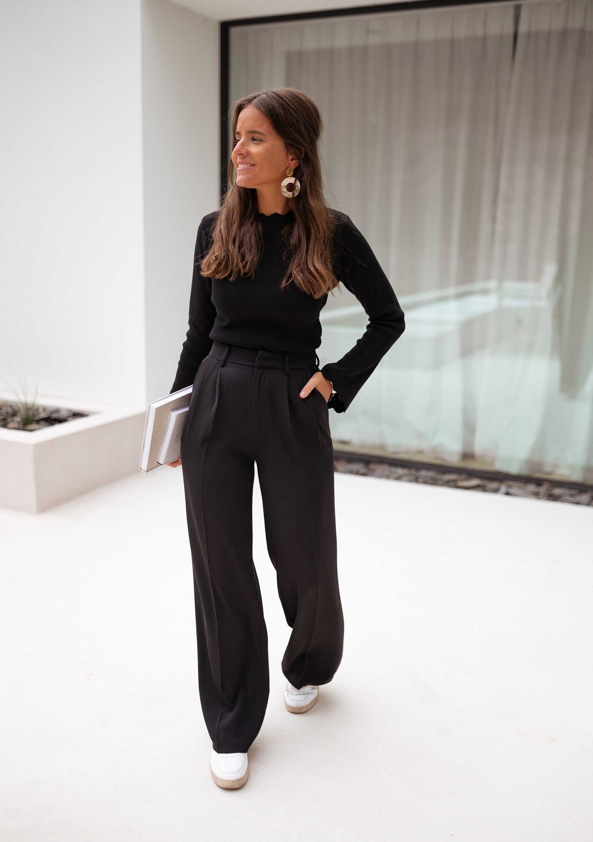 Pantalon à pinces noir porté par une femme, avec un haut noir, mains dans les poches