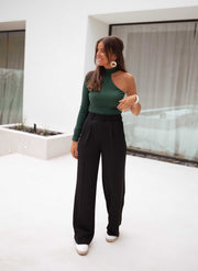Pantalon à pinces noir porté par une femme, avec un haut vert à col asymétrique