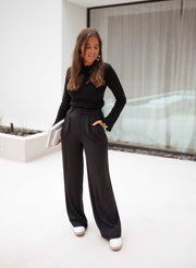 Pantalon à pinces noir porté par une femme, avec un haut noir à manches longues