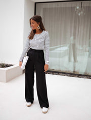 Pantalon à pinces noir porté par une femme, avec un haut rayé bleu et blanc