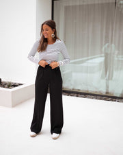 Pantalon à pinces noir porté par une femme, vue de trois-quarts, haut rayé, mains dans les poches